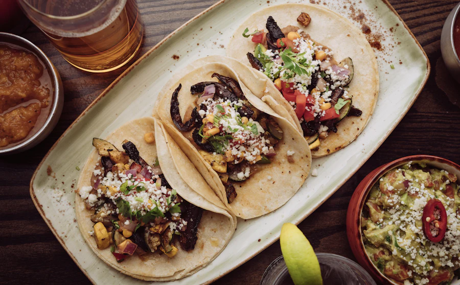Three loaded tacos on a platter with salsa and guacamole on a wood table
